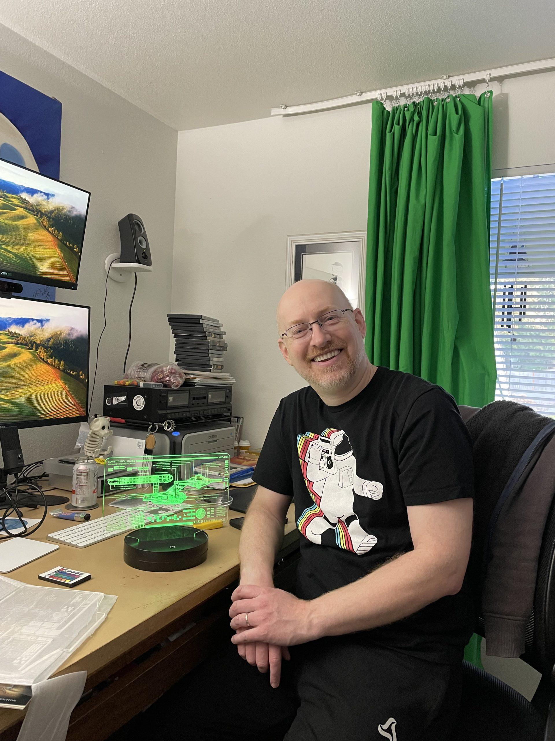 Me sitting at a somewhat messy desk next to a green-lit LED schematic of the original USS Enterprise.