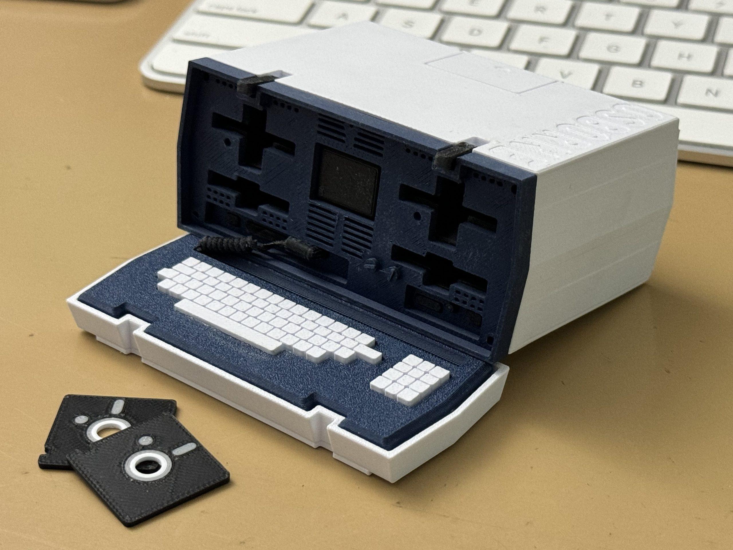 A small 3D printed Osborne 1 and two tiny floppy disks sitting on my desk in front of a modern Apple keyboard.