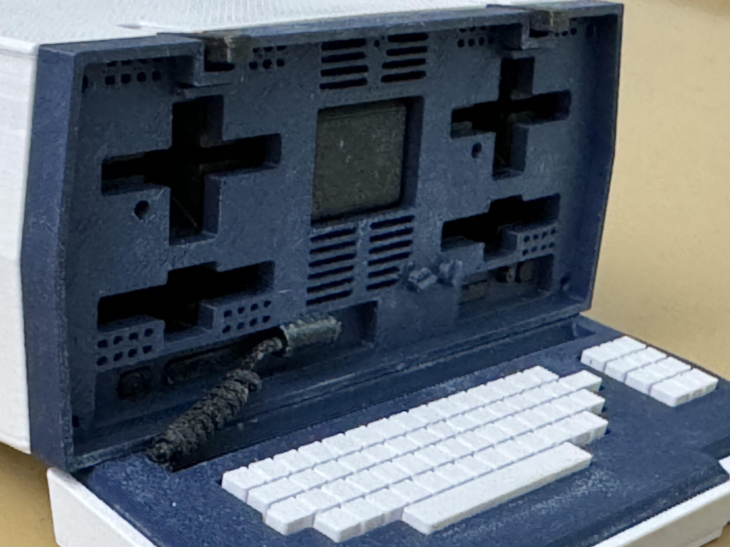 The front of the Osborne, showing the floppy drives, disk storage slots, screen, and keyboard connected to the case with a curly cable.