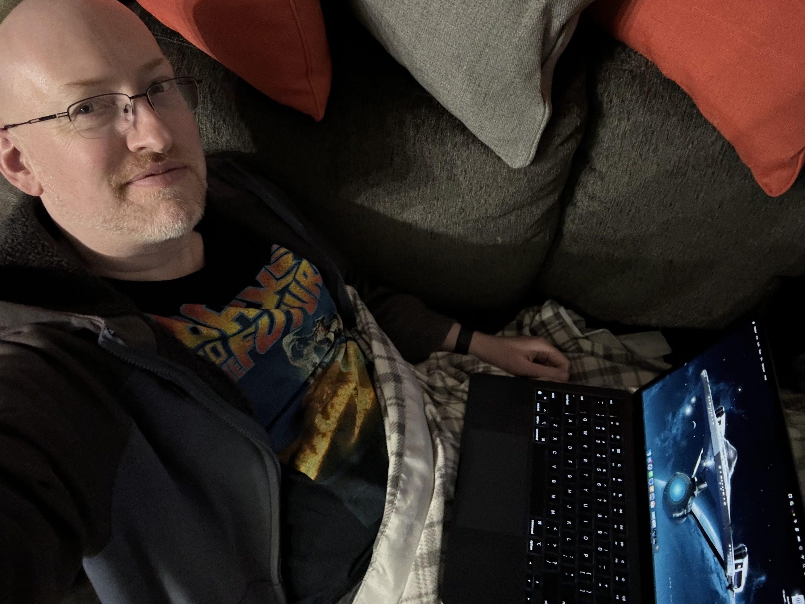 Me sitting on our couch with my computer on my lap. A desktop image of the orignal series USS Enterprise is visible on the screen.