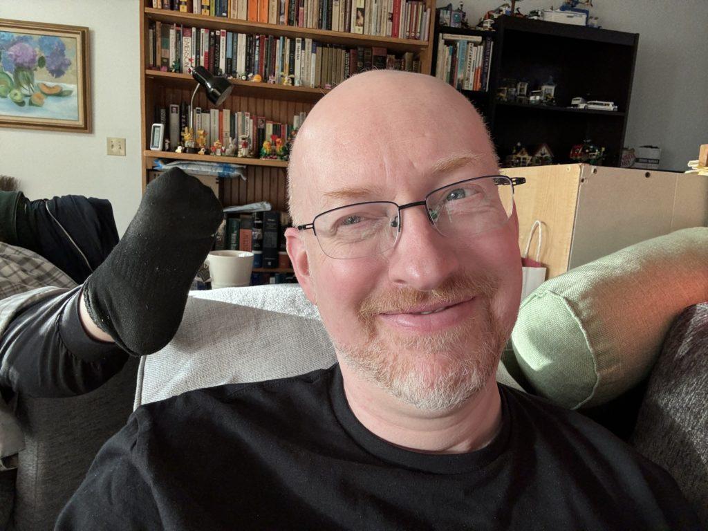 Me on the couch with a goofy amused smile, and with my wife’s foot next to my head.