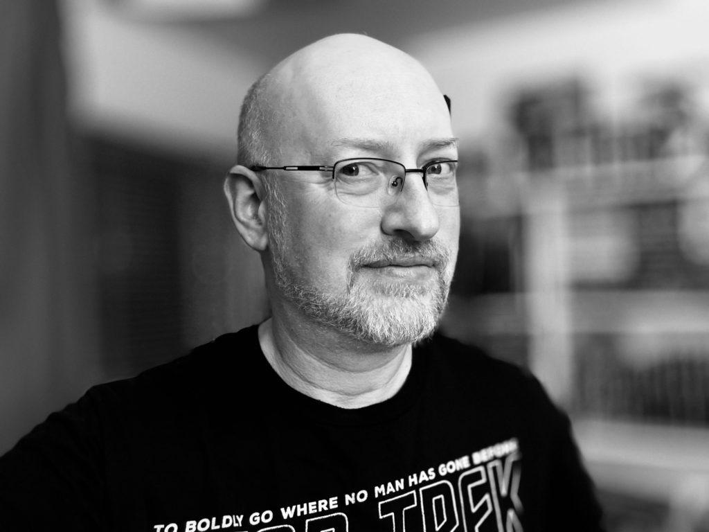 A black and white shot of me in my home office wearing a Star Trek t-shirt, with the background blurred out.