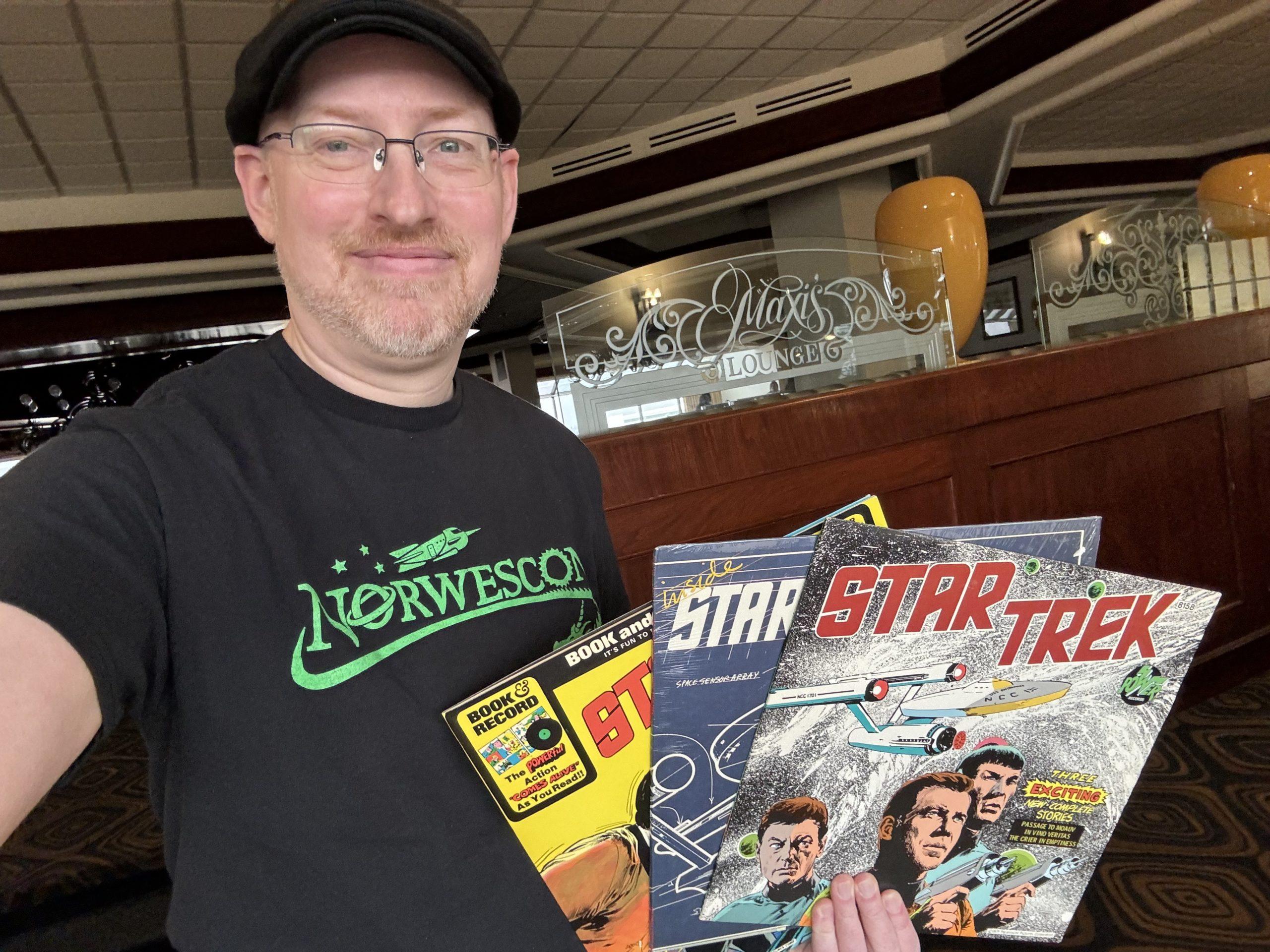 Me wearing a black t-shirt with the Norwescon logo in green, standing in Maxi's Lounge at the DoubleTree hotel, holding three old Star Trek LPs.