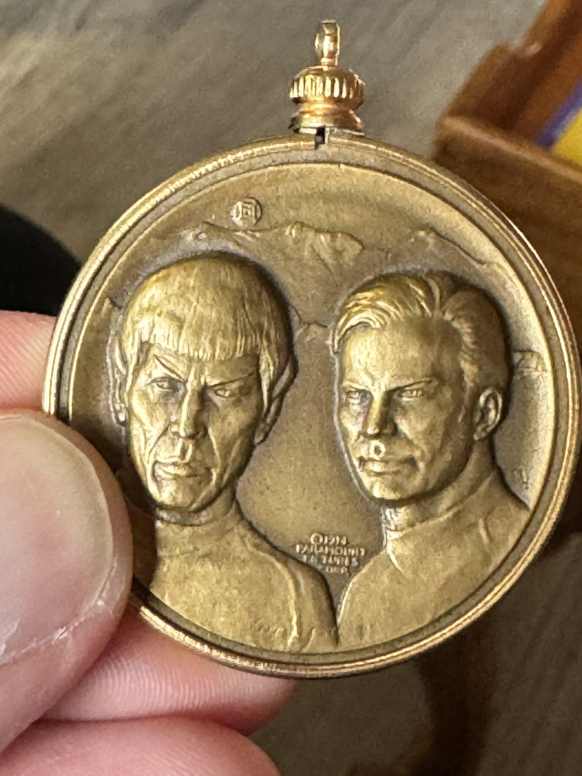 A bronze colored medallion a little over an inch in diameter molded with images of Kirk and Spock.