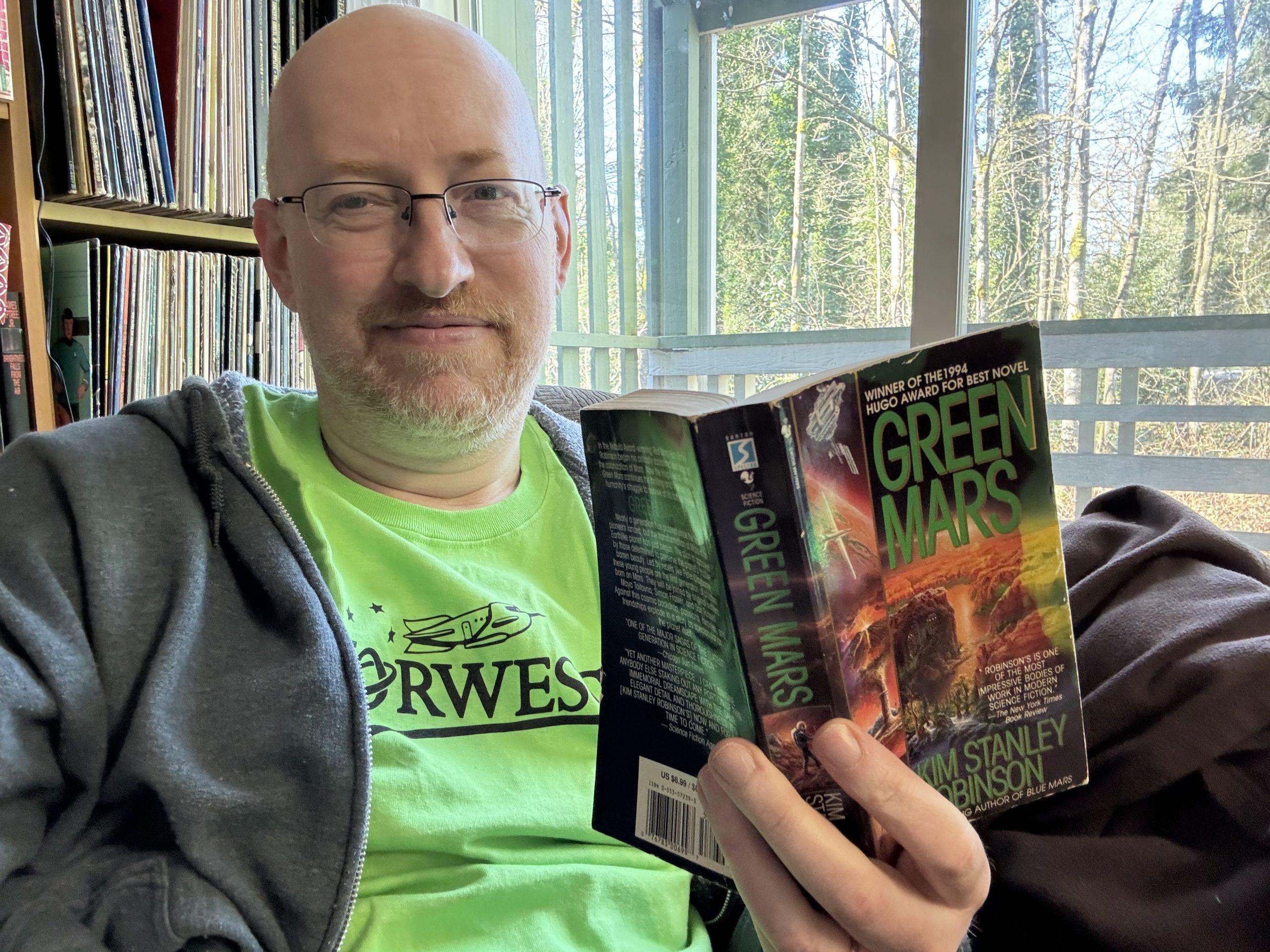Me wearing a bright green Norwescon shirt and holding Kim Stanley Robinson's book Green Mars.