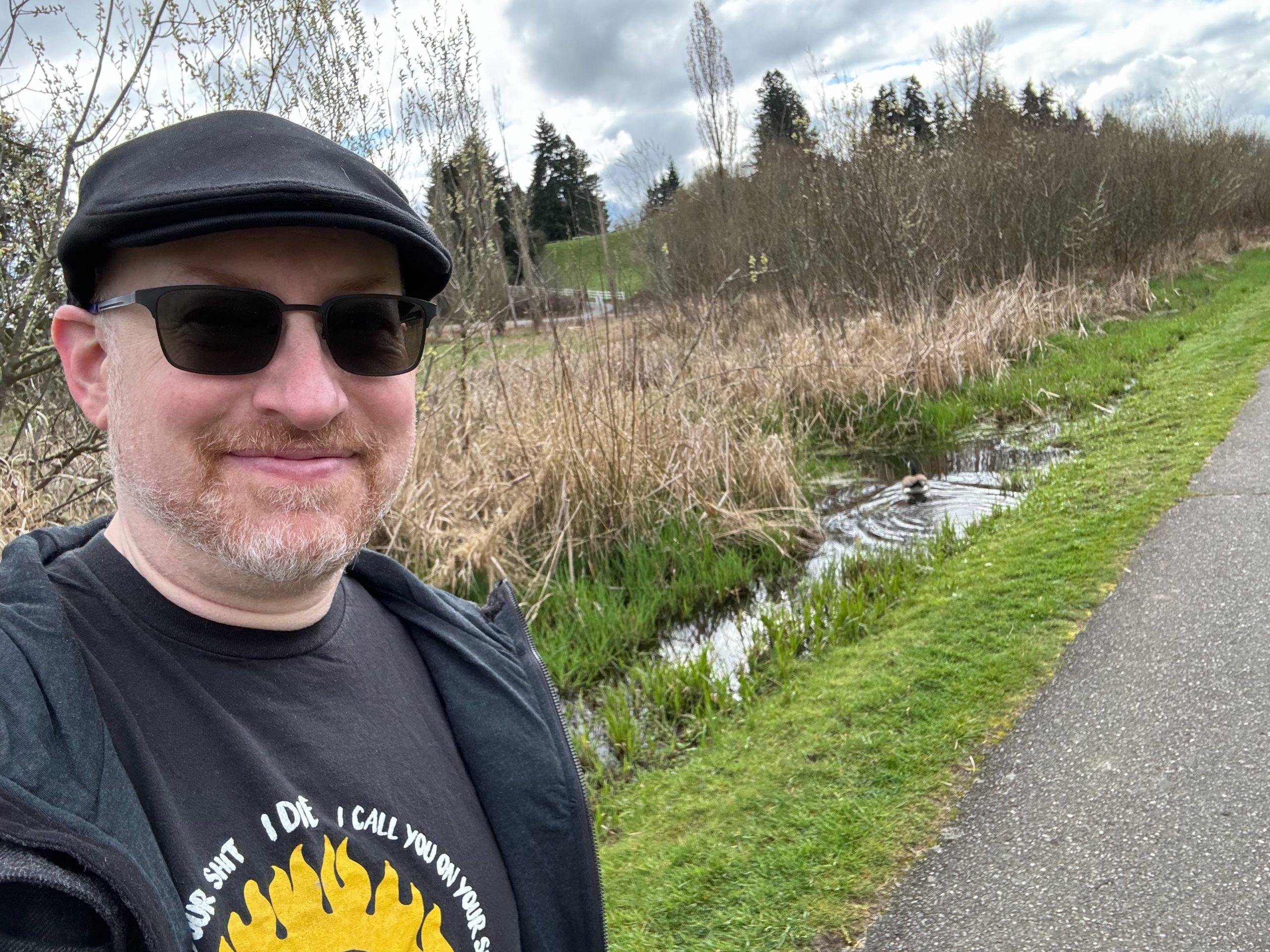 Me on a path next to marshland, with a Canadian Goose visible in a pond just behind me.