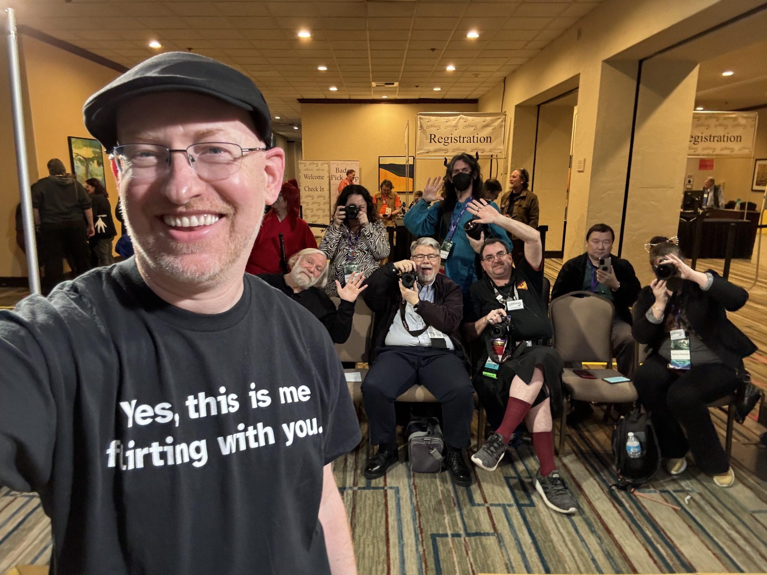 Me wearing a shirt that says 'yes, this is me flirting with you', standing in front of a group of convention photographers with their cameras aimed at me.