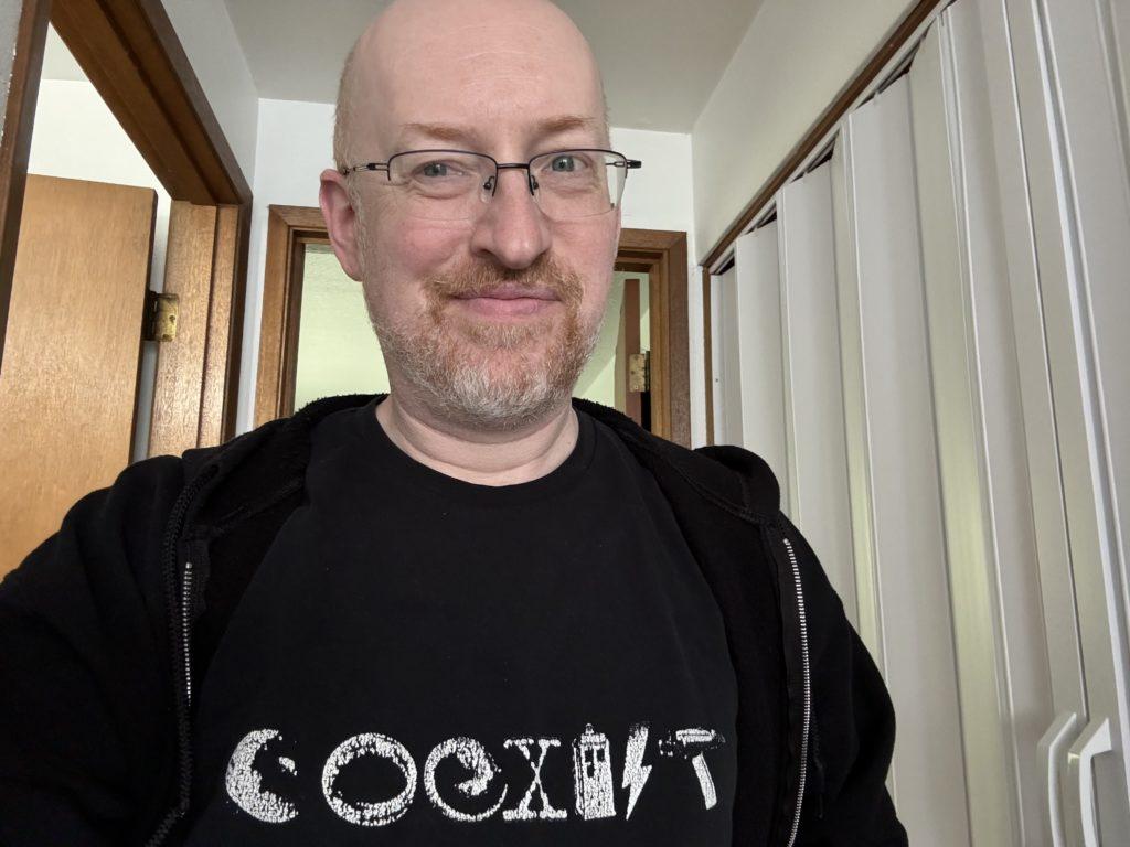 Me wearing a black t-shirt with the word ‘coexist’ made up of objects and symbols from several science fiction and fantasy franchises.