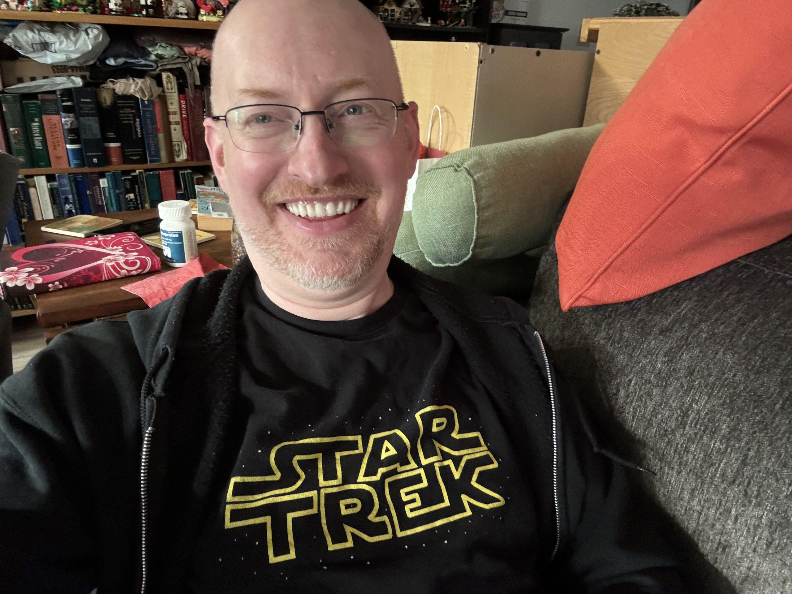 Me on my couch, wearing a shirt that says "Star Trek" but uses the Star Wars logo font and design.