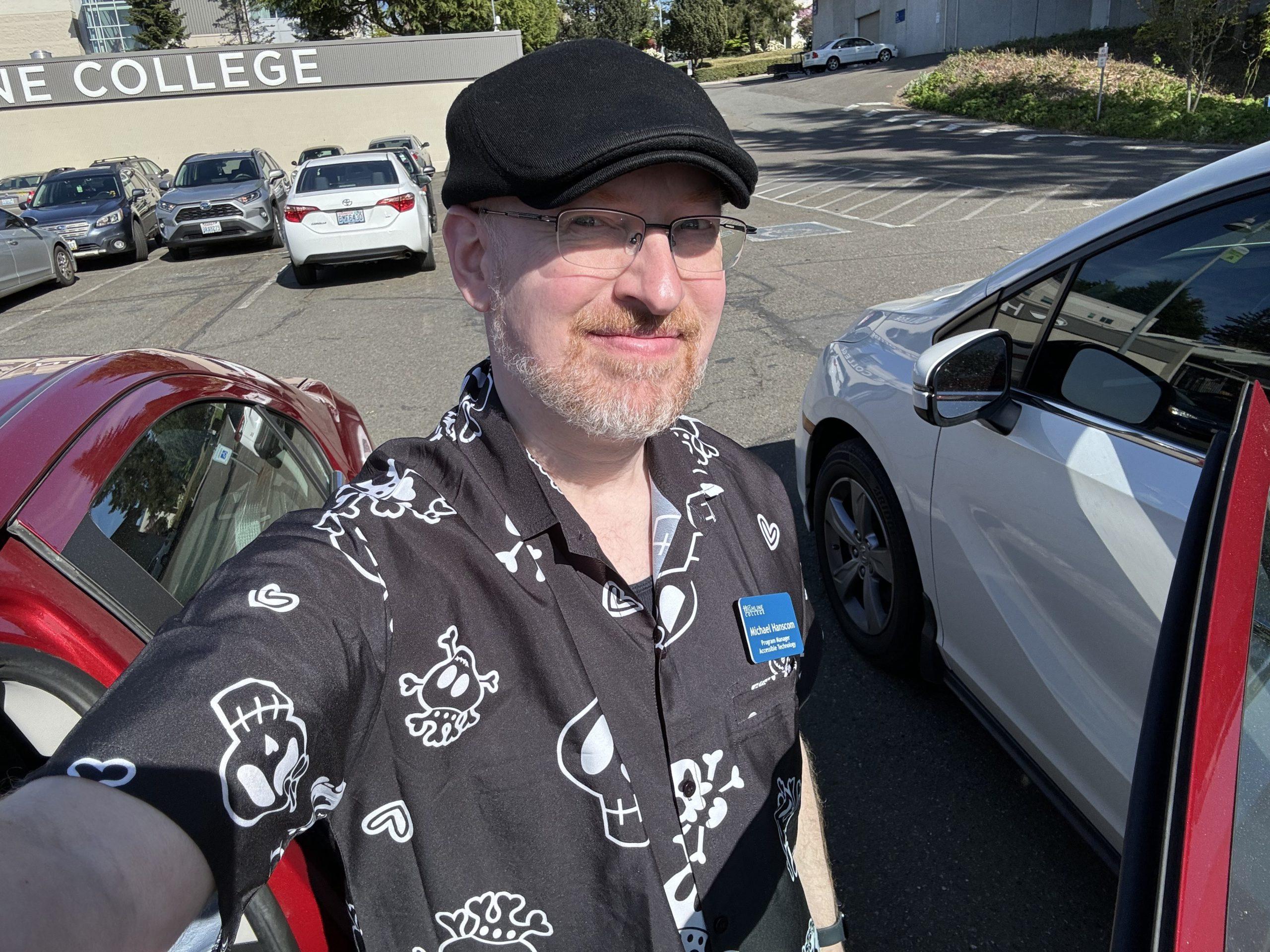 Me in the college parking lot by my car, standing in the sun, wearing a shirt with very cute cartoon skulls.
