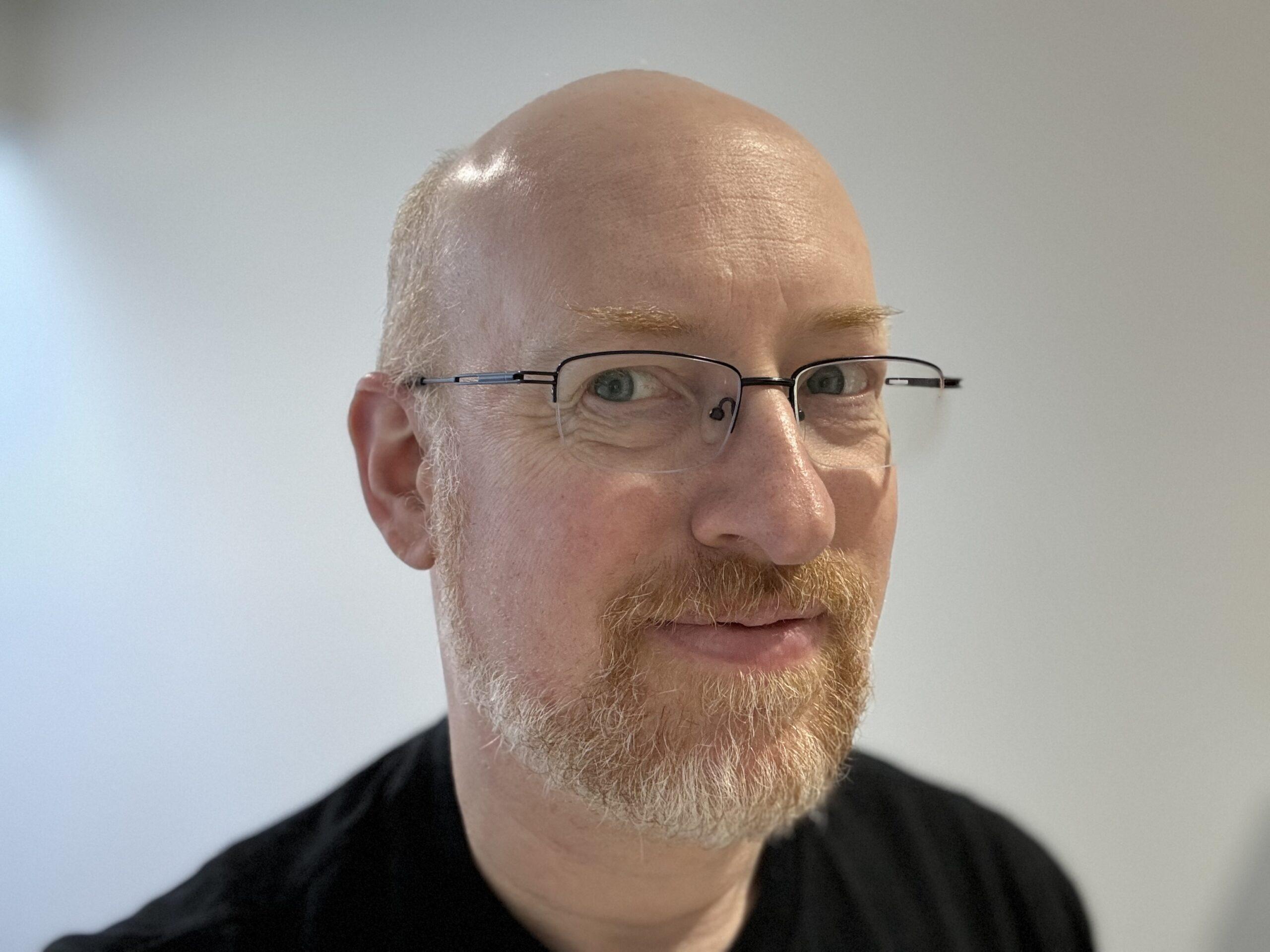 Me, a white man, bald, with greying red beard, wearing glasses and a black t-shirt, against a white background.