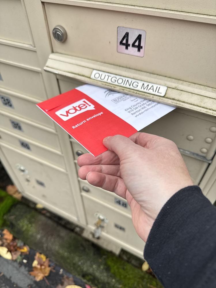 My hand placing my ballot envelope in the outgoing mail slot of our neighborhood mailbox.