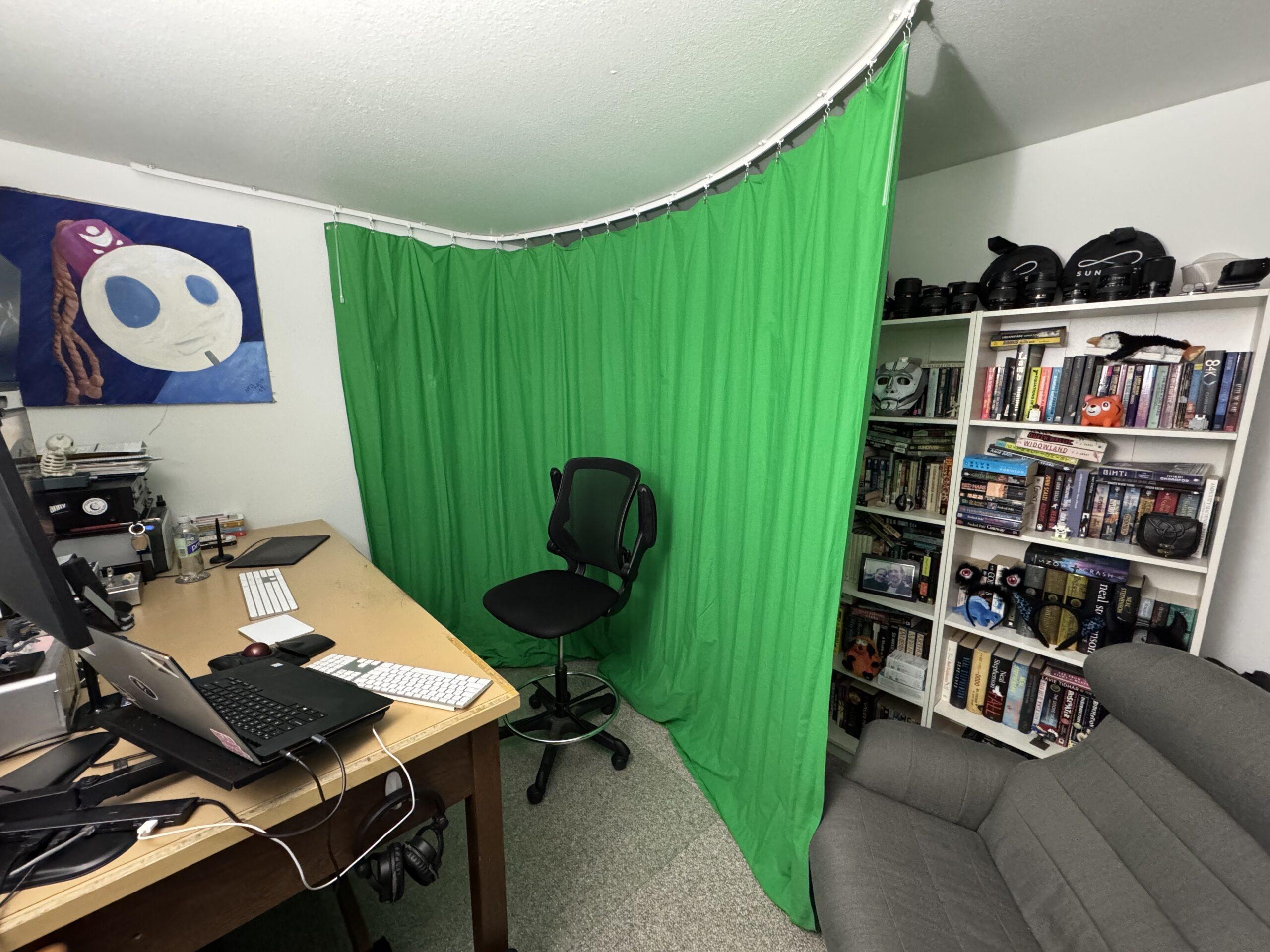 The same view as before, only now the green curtain has been pulled along the ceiling track to form a curved green screen between the desk and the bookshelves.