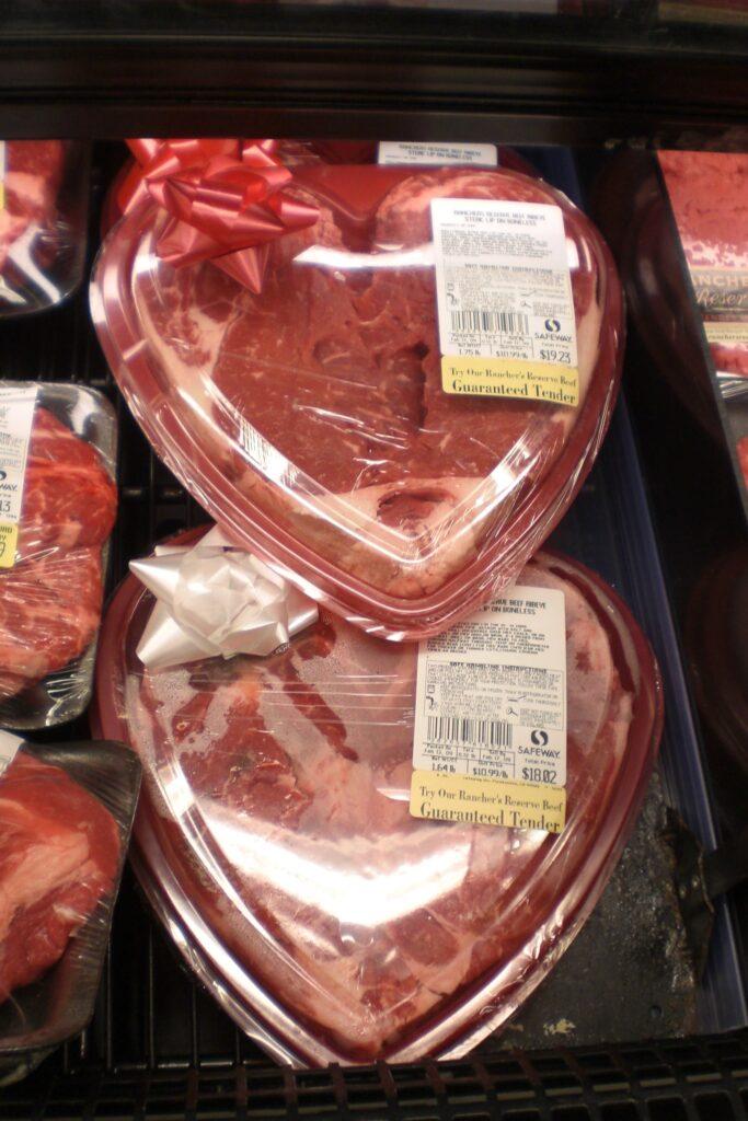 Steaks in heart-shaped containers with bows attached in a grocery store meat display case.