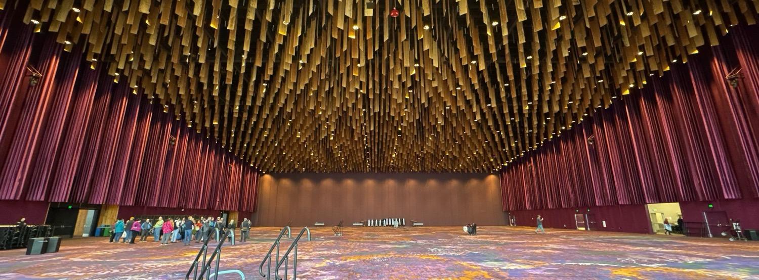 A wide-angle shot of a huge convention center ballroom, with maroonish side walls and a high ceilig with a pattern that's formed by hanging planks of wood.