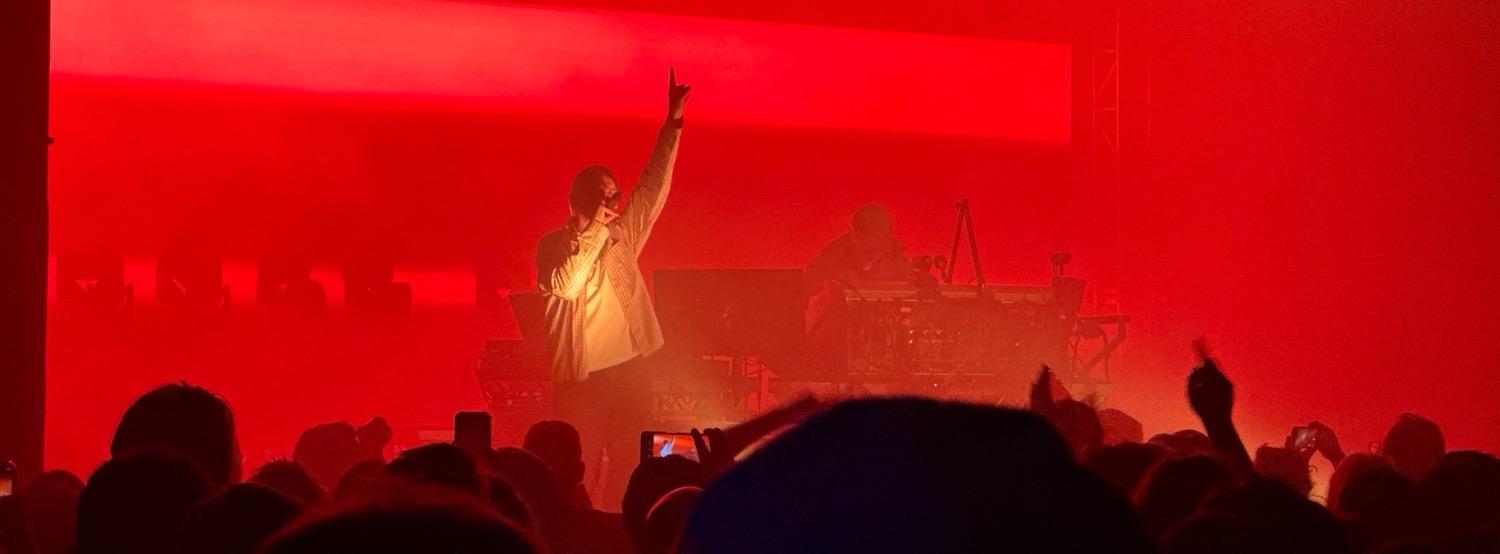 Underworld performing, with Karl Hyde singing and pointing to the sky, lit all in reds.