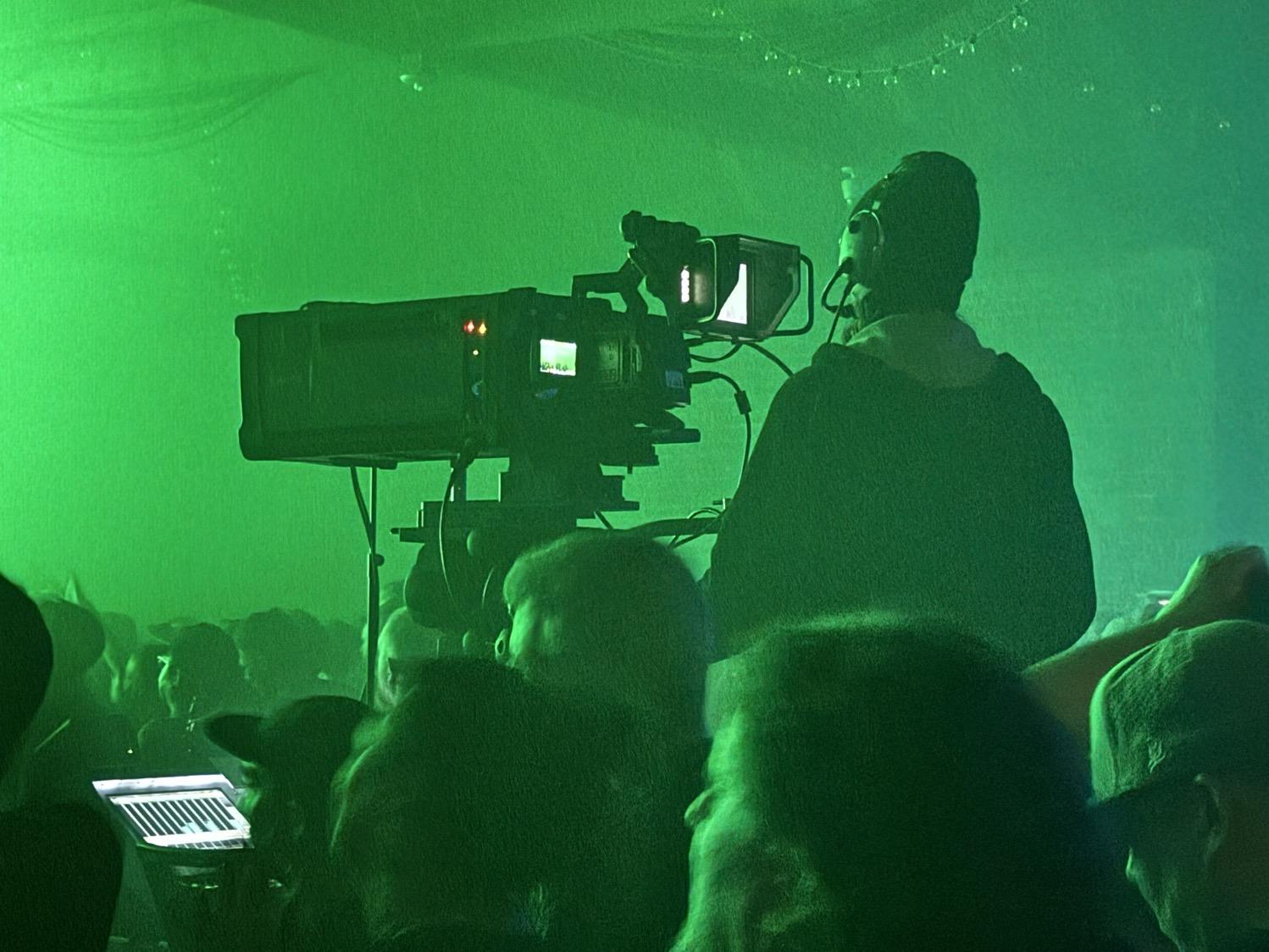 A camera person using a large professional camera during the Underworld concert, with everything lit in green.