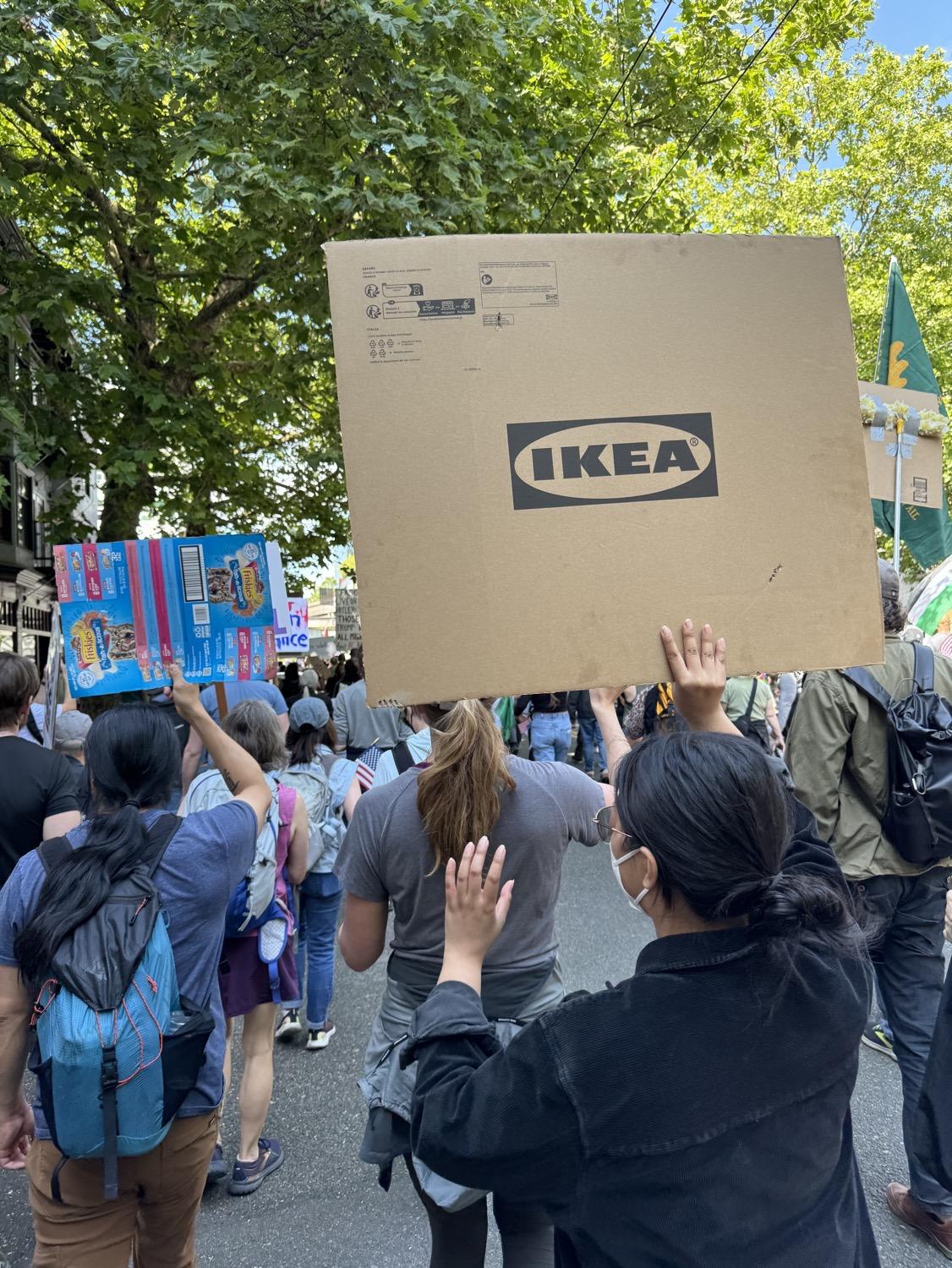 Seen from behind, a marcher holds up a large piece of cardboard with the IKEA logo.