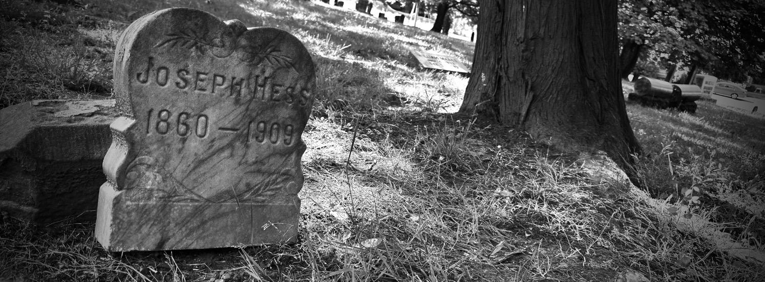 Black and white photo of a gravestone from 1909 next to a tree.
