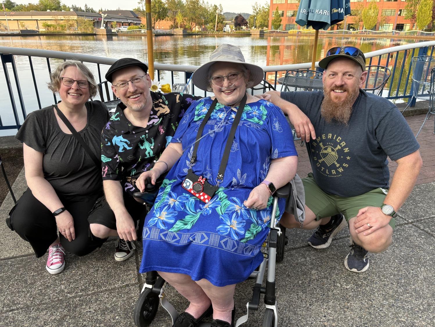 IMG_9932.jpeg My wife, me, and my brother, all crouched on either side of my mom in her motorized chair in front of a human-made lake.