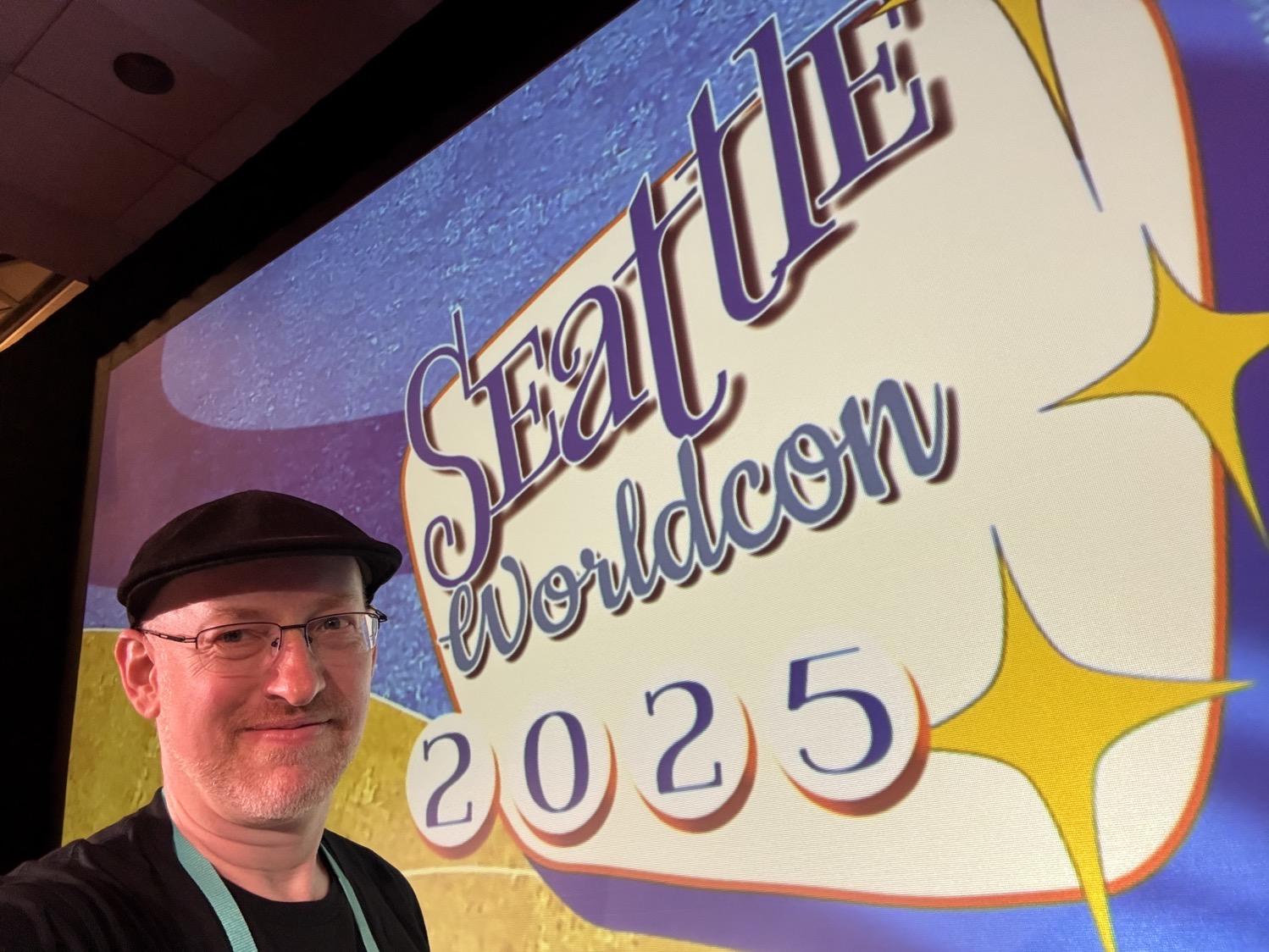 IMG_4692.jpeg Me in front of a big screen showing the Seattle Worldcon logo.