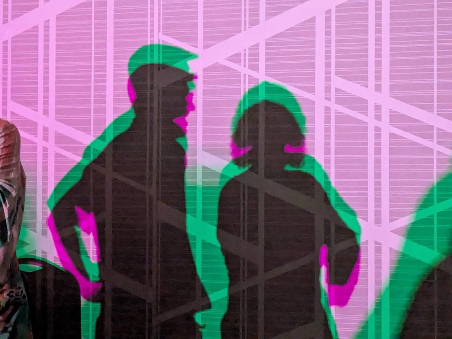 IMG_4739.JPG Layered silhouettes of two people talking, in dark pink and green against a light pink lit wall.