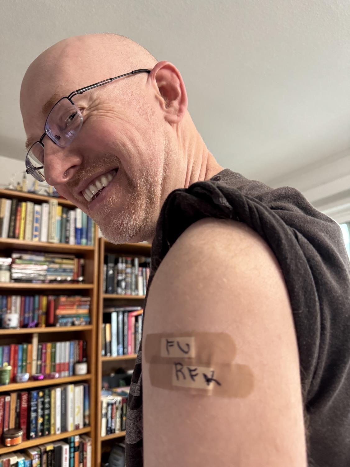 Me with the left sleeve of my t-shirt rolled up to reveal two band-aids that have been written on with black permanent marker; the top says "F U" and the bottom says "R F K".