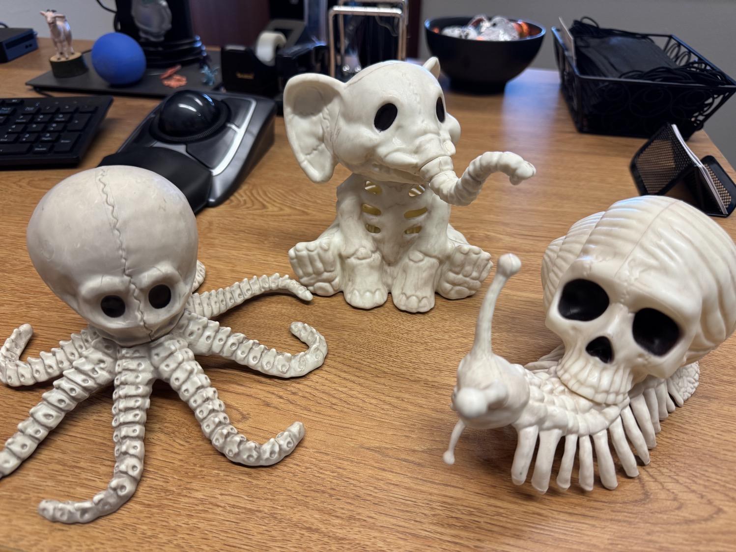 Three decorative 'skeleton' creatures on my office desk. One is an elephant (complete with solid bone ears and trunk bones), one an octopus (with large skull and tentacle bones), and one a snail (with skull shell, solid antennae, and a bony ribcage-like structure for the foot that makes it look almost centipedal).
