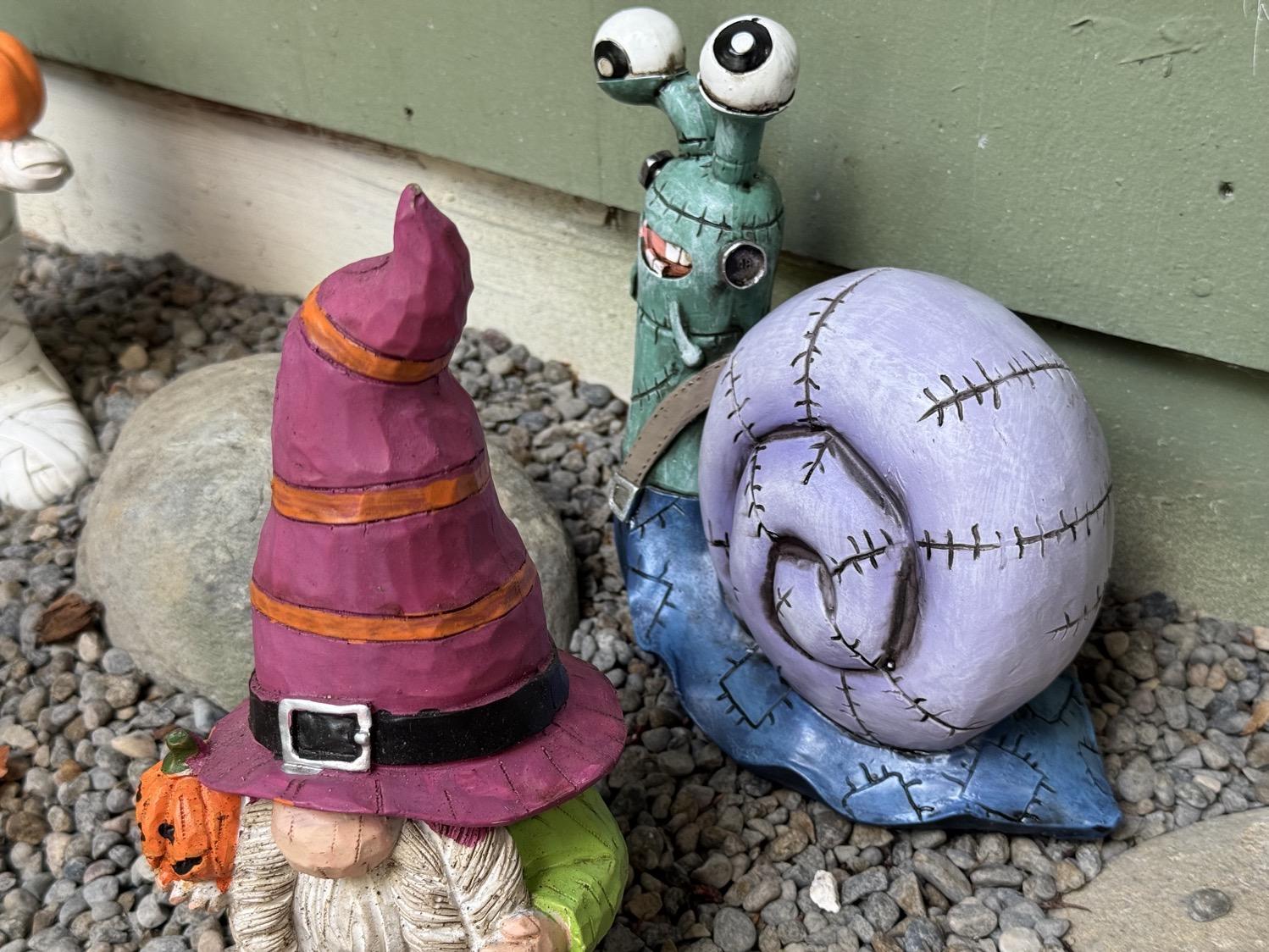 An outdoor figurine of a snail with a green head, blue foot, and purple shell, all stitched up and with metal plugs like Frankenstein's monster.