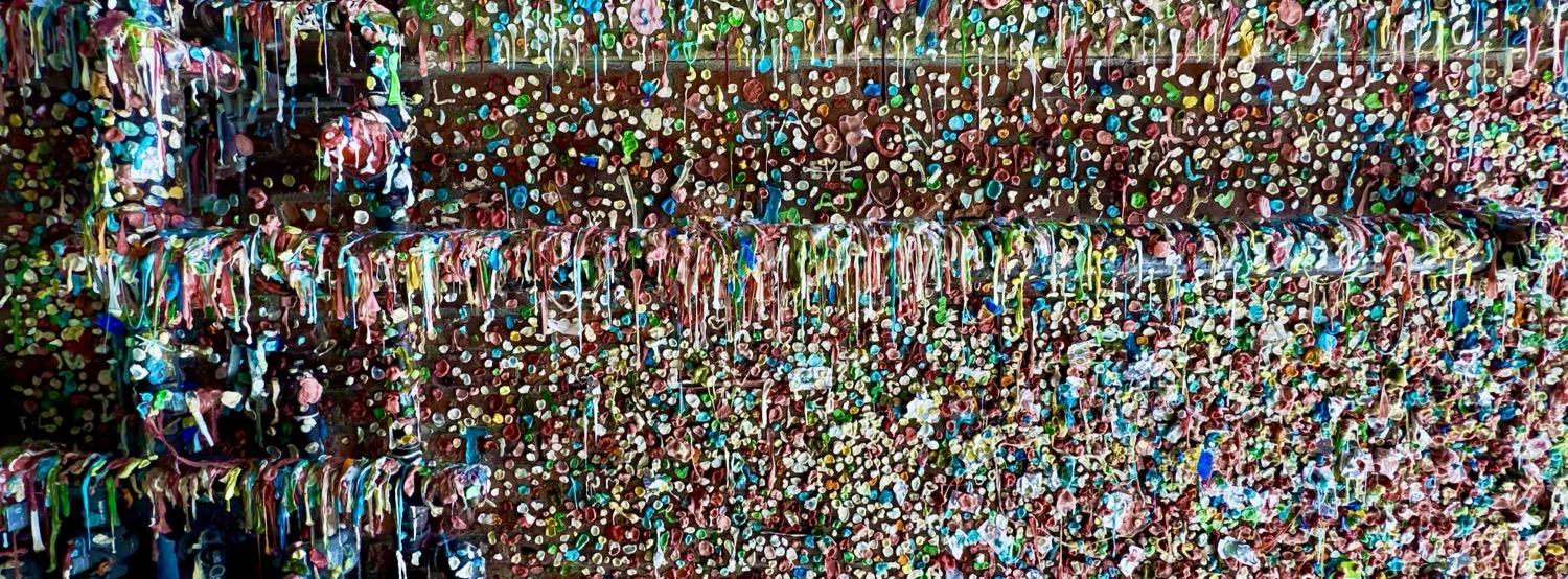 A section of brick wall and utility pipe barely visible behind hundreds of pieces of used, chewed gum, some stuck to the wall in blobs, some stretched to hang off of the pipes. It's actually more gross than it sounds.
