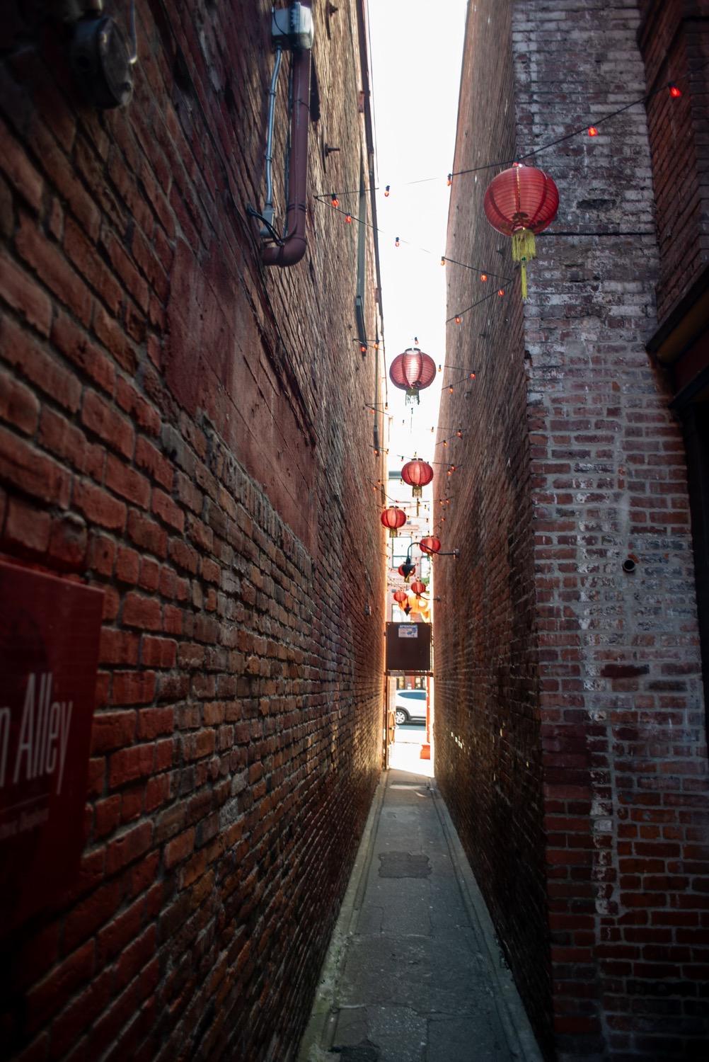 A narrow brick alley, strung with lights and round red paper lanterns.