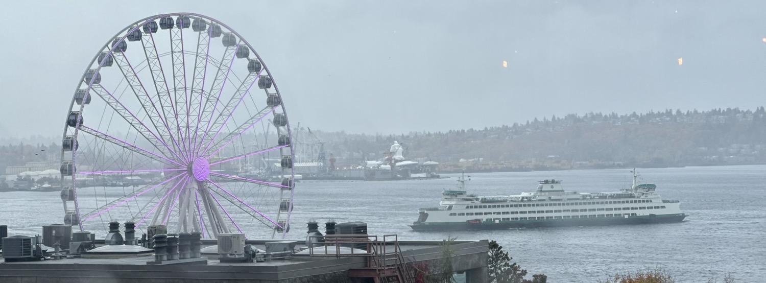 A Washington state ferry pulls in with the Seattle waterfront ferris wheel in the foreground on a grey fall day.
