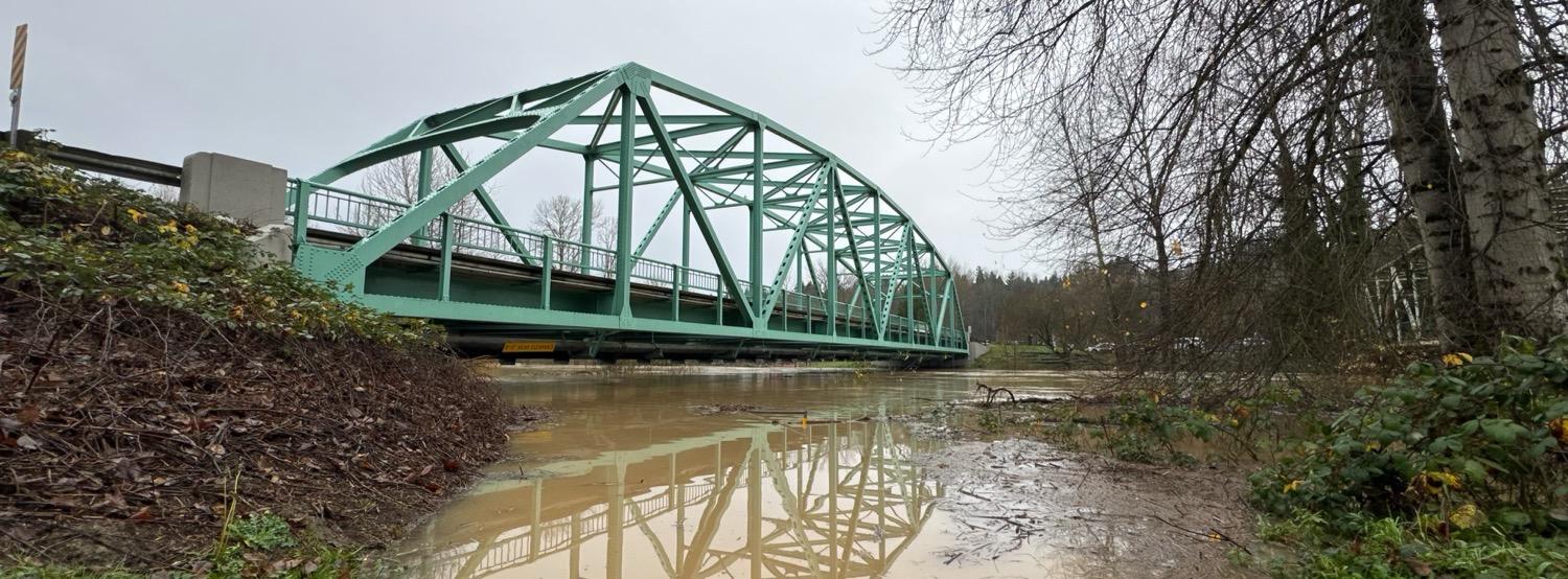 IMG_5462.jpeg A green painted steel bridge over a river well over its normal banks; an “8’ Head Clearance” can be seen under the bridge just a couple feet above the water level.