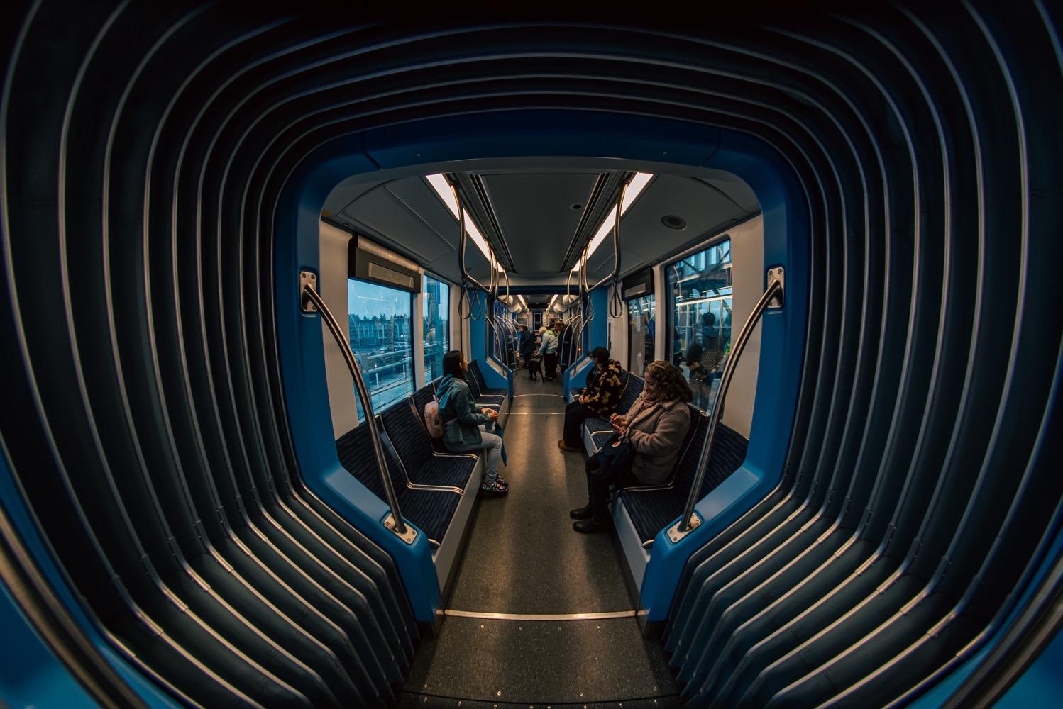 Light Rail Federal Way Extention Accessibility Tour - 029.jpg A fisheye view inside a light rail train. A flexible section in the foreground is distorted to appear like a much larger tunnel, with passengers on seats stretching away into the far distance.
