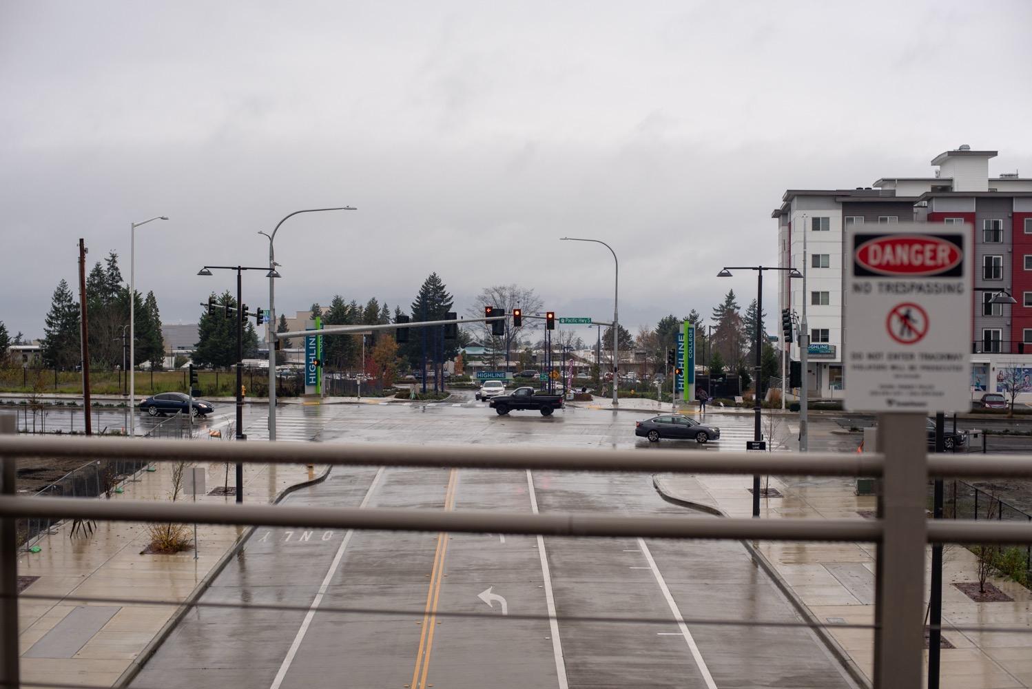 Light Rail Federal Way Extention Accessibility Tour - 049.jpg A city street on a rainy day from the elevated platform of the light rail. Visible in the distance are the blue-and-green signs marking the entrance to Highline College.