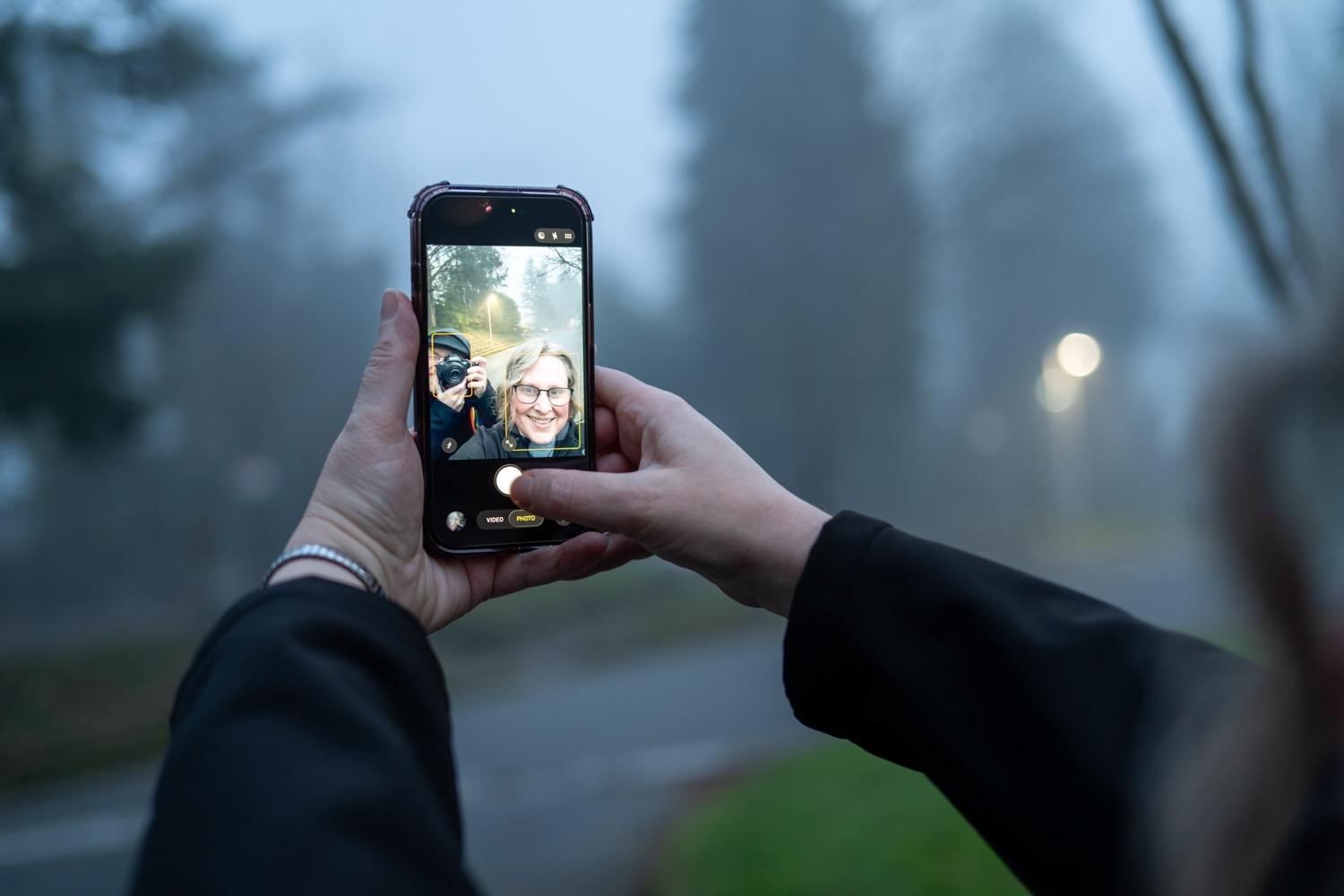 - 005.jpg My wife's outstretched arms hold an iPhone taking a selfie, with her smiling face and me holding up my camera in front of my face visible on the iPhone's screen.