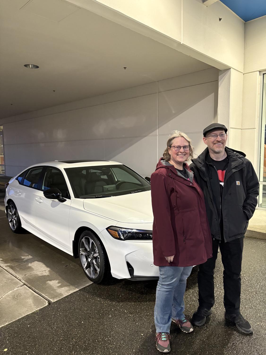My wife and I stand in front of a brand new white four-door Honday Civic.