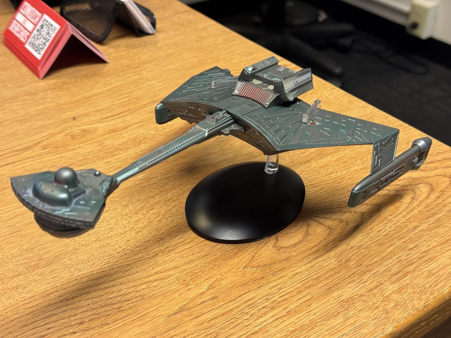 A model of a Klingon K'Tinga class battlecruiser, sitting on a wooden desk.