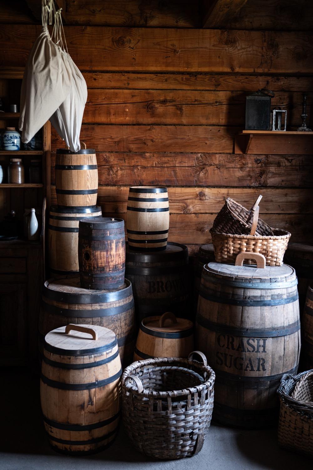 Barrels of supplies are stacked in an old pantry, all lit by natural light, looking almost like a painted still life.