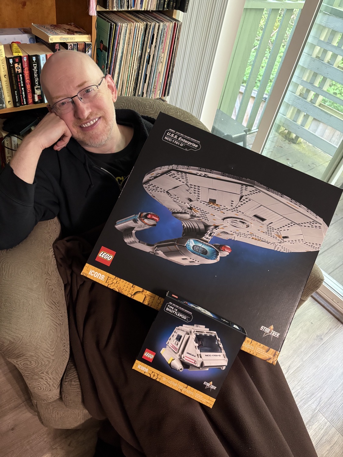 Me sitting on a chair in our living room, holding the giant box of the Lego Enterprise D and the smaller box of the Onizuka shuttle on my lap.