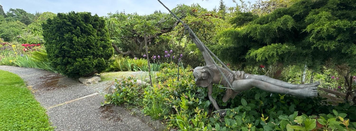 A wide aspect shot of a garden with a bronze sculpture of a young girl swinging on a rope swing.