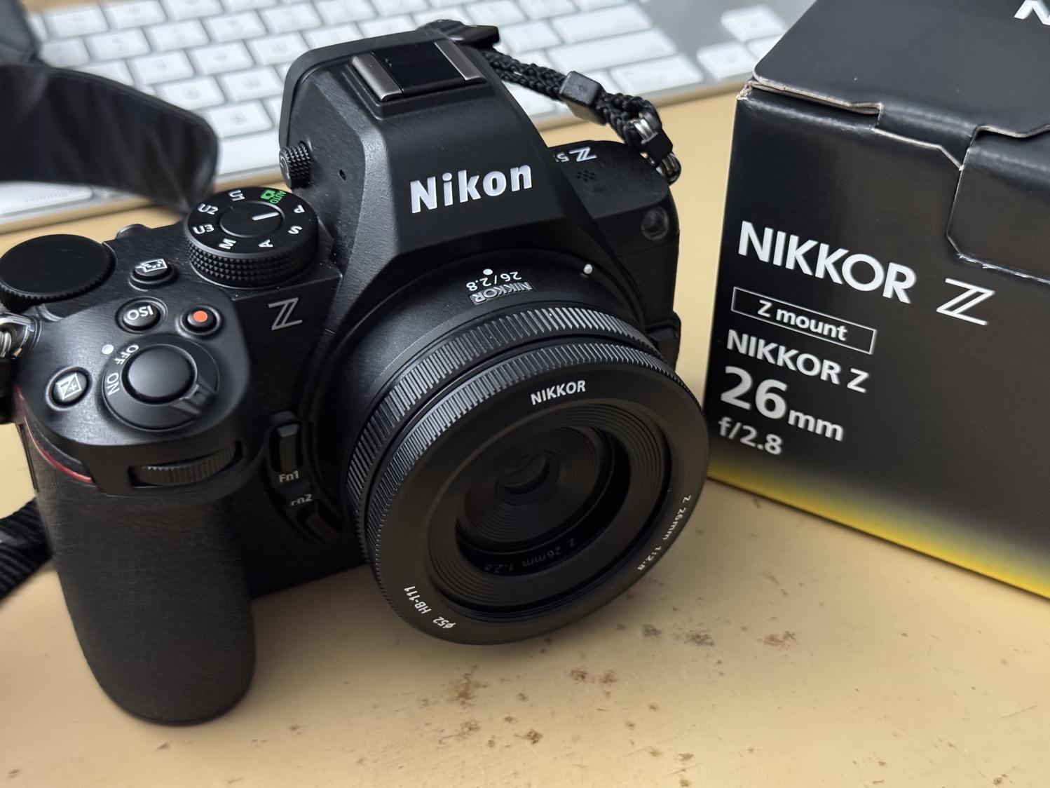 IMG_6225.jpeg A Nikon Z5ii camera with a small (nearly 'pancake' style) Nikkor 26mm wide-angle lens attached, sitting next to the box for the lens.