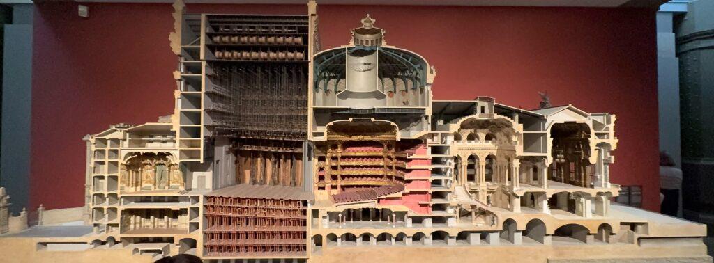 A large diorama model of the Paris Opera, cut down the middle to show the layout and construction of the building’s sections, including the stage and its above- and below-stage mechanics, the theater with its seats and balconies, and the entrance and lobby with its grand staircase.