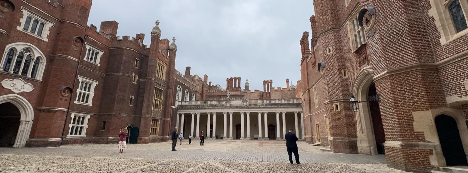 Panoramic shot of a cobblestone courtyard with large brick walls to either side and a columned walkway along the far side.