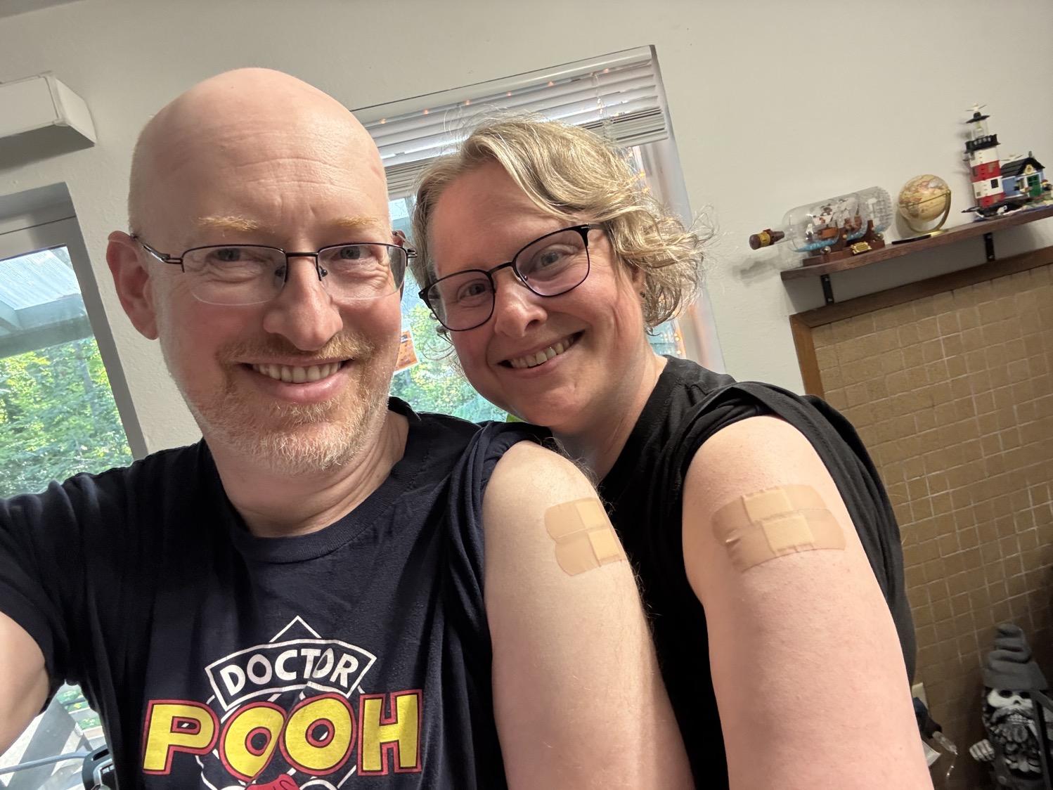 Selfie of my wife and I with our left shirt sleeves pulled up to show each of us with two bandaids on our upper arms.
