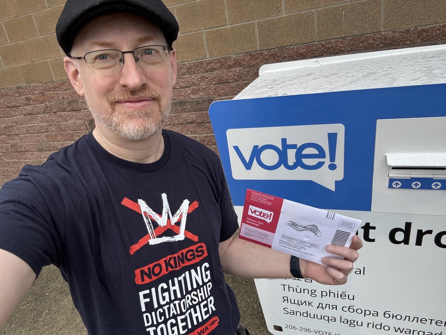 IMG_7302.jpeg A selfie of me wearing a No Kings shirt and holding my ballot in front of a ballot drop box.